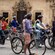 People standing by bicycles in front of a building featuring flags, a clock, windows and more